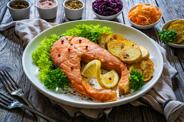 Fried salmon steak with potatoes and fresh vegetable salad served on wooden table
