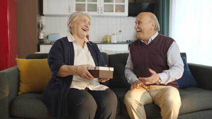 Happy mature old man giving a gift box to his wife. An elderly woman is shocked to receive a gift...