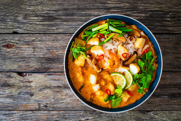 Tom Yum - Thai soup with halibut nuggets and rice noodles on wooden table

