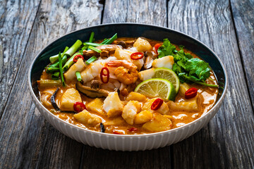 Tom Yum - Thai soup with halibut nuggets and rice noodles on wooden table
