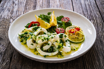 Fried calamari rings with lemon, greens and cherry tomatoes on wooden table
