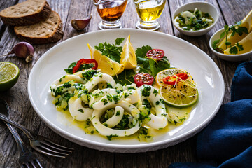 Fried calamari rings with lemon, greens and cherry tomatoes on wooden table
