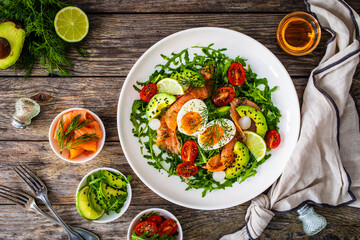 Salmon salad - smoked salmon, hard boiled eggs, avocado and leafy greens on wooden table
