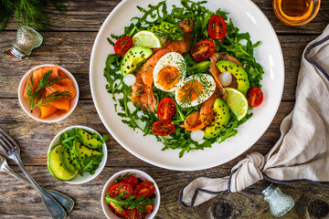 Salmon salad - smoked salmon, hard boiled eggs, avocado and leafy greens on wooden table
