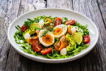 Salmon salad - smoked salmon, hard boiled eggs, avocado and leafy greens on wooden table
