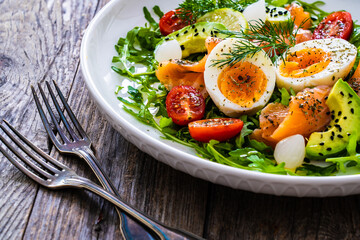 Salmon salad - smoked salmon, hard boiled eggs, avocado and leafy greens on wooden table
