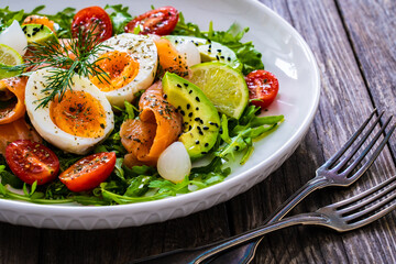 Salmon salad - smoked salmon, hard boiled eggs, avocado and leafy greens on wooden table
