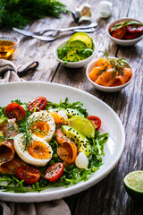 Salmon salad - smoked salmon, hard boiled eggs, avocado and leafy greens on wooden table
