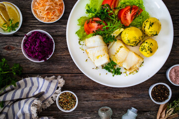 Fish dish - fried halibut with boiled potatoes and fresh vegetables on wooden table
