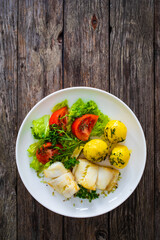 Fish dish - fried halibut with boiled potatoes and fresh vegetables on wooden table
