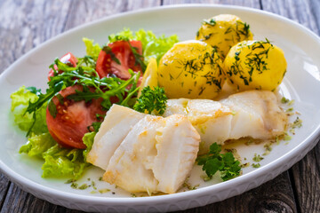 Fish dish - fried halibut with boiled potatoes and fresh vegetables on wooden table
 - obrazy, fototapety, plakaty