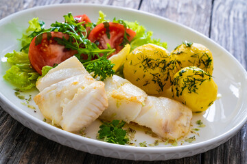 Fish dish - fried halibut with boiled potatoes and fresh vegetables on wooden table
