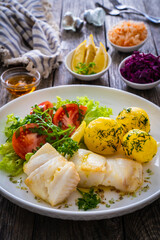 Fish dish - fried halibut with boiled potatoes and fresh vegetables on wooden table

