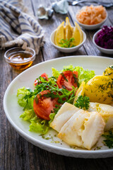 Fish dish - fried halibut with boiled potatoes and fresh vegetables on wooden table
