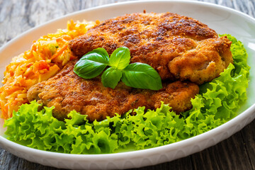 Breaded fried pork chop with cabbage salad and greens on wooden table
