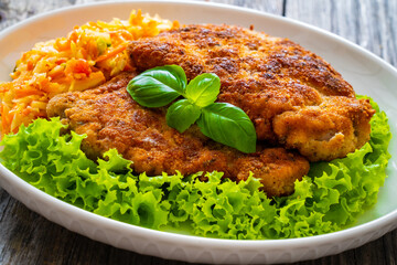 Breaded fried pork chop with cabbage salad and greens on wooden table
