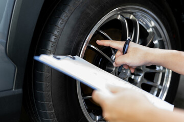Fototapeta na wymiar Car business concept, Insurance staff check for damage to the wheels of the car from an accident and record the details in the claim document so that customers are satisfied with the service