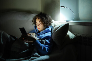 A warmly dressed teenage girl uses a smartphone in a dark room without electricity and heating with...