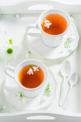 Two cups of tea served on white tray with flowers.