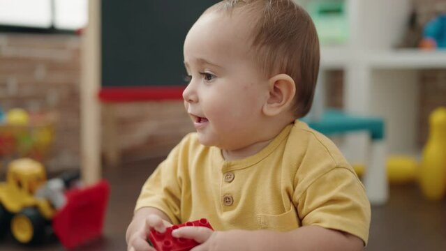 Adorable hispanic baby playing with construction blocks sitting on floor at kindergarten
