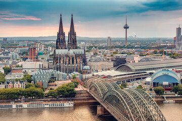 Cologne Aerial view with trains move on a bridge over the Rhine River on which cargo barges and passenger ships ply. Majestic Cologne Cathedral in the background