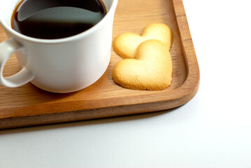 Heart-shaped biscuits with a mug of coffee on a wooden tray and placed on a white floor, Valentine's day concept.