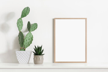 Empty vertical frame mockup in modern minimalist interior with plant in trendy vase on white wall...