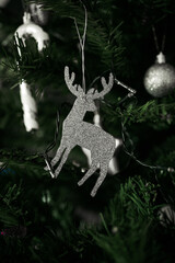 Sparkling Christmas deer with antlers, silver colored glittering holiday reindeer ornament hanging in artificial Christmas tree, selective focus macro shot - 552828017