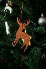 Sparkling Christmas deer with antlers, copper colored glittering holiday reindeer ornament hanging in artificial Christmas tree, selective focus macro shot - 552828024