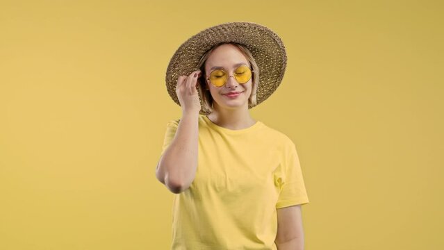 Playful blonde woman smiling, flirting to camera on yellow studio background. Cute trendy girl corrects her hair.