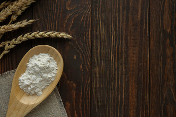 Ears of wheat and white flour in a spoon on a dark wooden background with space for text
