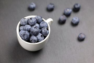 Fresh blueberries in a white cup and scattered on dark table. Natural berries background