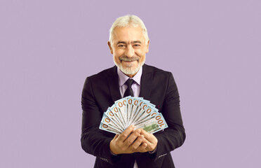 Wealthy and successful. Happy mature man in formalwear holding dollar bills isolated on pastel...