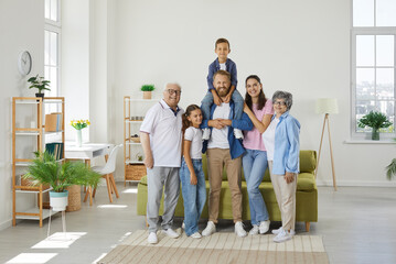 Happy family poses for the camera in a large bright cozy room. The son is on the shoulders of the...