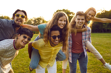 Young friendly multiracial people from high school, friends relaxing in summer park and giving each...