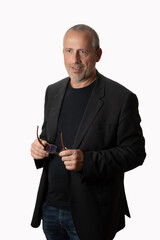 Middle-aged manager in casual suit standing before an isolated background, holding glasses, looking sidewards, smiling