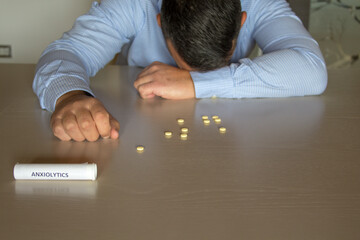 Image of a man with his head resting on the table and a tube of anxiolytics and medicines scattered...