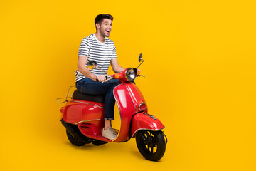 Fototapeta na wymiar Full length photo of carefree excited man wear white t-shirt driving bike looking empty space isolated yellow color background