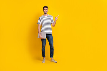 Fototapeta premium Full length photo of sweet charming man wear white t-shirt holding modern gadget pointing empty space isolated yellow color background