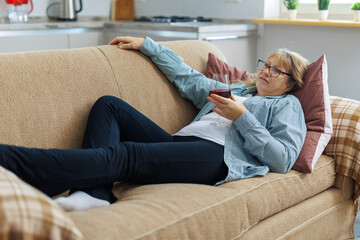 Elderly woman 50s years old wears casual clothes lies on sofa use laptop computer watch movie film...