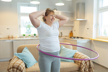 Overweight mature woman in white t-shirt and gray leggings trying to lose weight with hula hoop exercises © SOLOTU