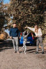 Fototapeta premium Man with woman have fun with their dog outdoors in forest near car.