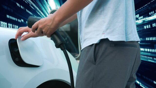 Progressive man charge electric car with power cable plug from charging station with technology background of binary code flying through votex. EV car concept with modern technology.