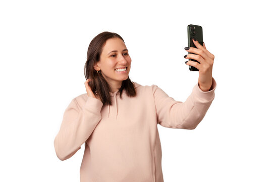 Young smiling shy woman wearing a hoodie is taking a selfie while gentle touching her hair.