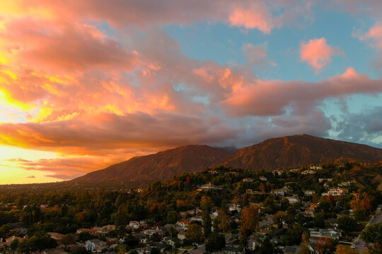 aerial shot of majestic mountains with powerful clouds and blue sky with homes, apartments and lush green trees at sunset in Monrovia California USA
