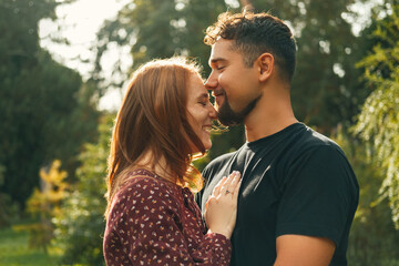 Cheerful young man kisses his woman on forehead while embracing in the park on a sunny day.