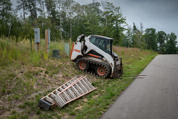 Mini front end loader with forklift attachment parked next to a paved street with two ladders, at a new home construction site.