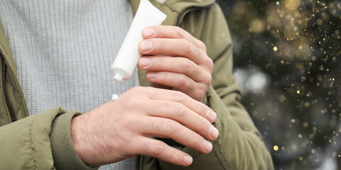 Man applying cream from tube onto hand outdoors, closeup. Winter care. Banner design
