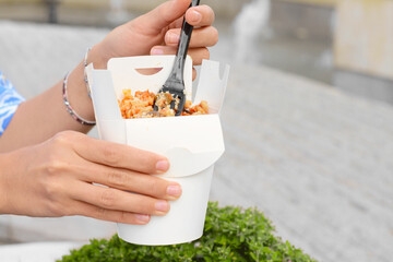 Woman eating takeaway noodles from paper box with fork outdoors, closeup and space for text. Street...