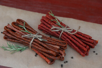 Tasty dry cured sausages (kabanosy) and spices on parchment paper